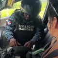 En un audiovisual, el uniformado se encuentra junto a la puerta del pasajero de un vehículo, manipulando las pertenencias de una dama que, al parecer, es de nacionalidad norteamericana. Mientras eso ocurre, la extranjera observa con asombro la acción y, al mismo tiempo, utiliza su teléfono celular para filmar.