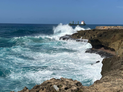 Un choque dramático entre el mar implacable y la tierra sólida. Las olas turquesas rompen furiosamente contra una costa rocosa de textura rugosa, creando una ráfaga de espuma blanca. ,. Jorge González