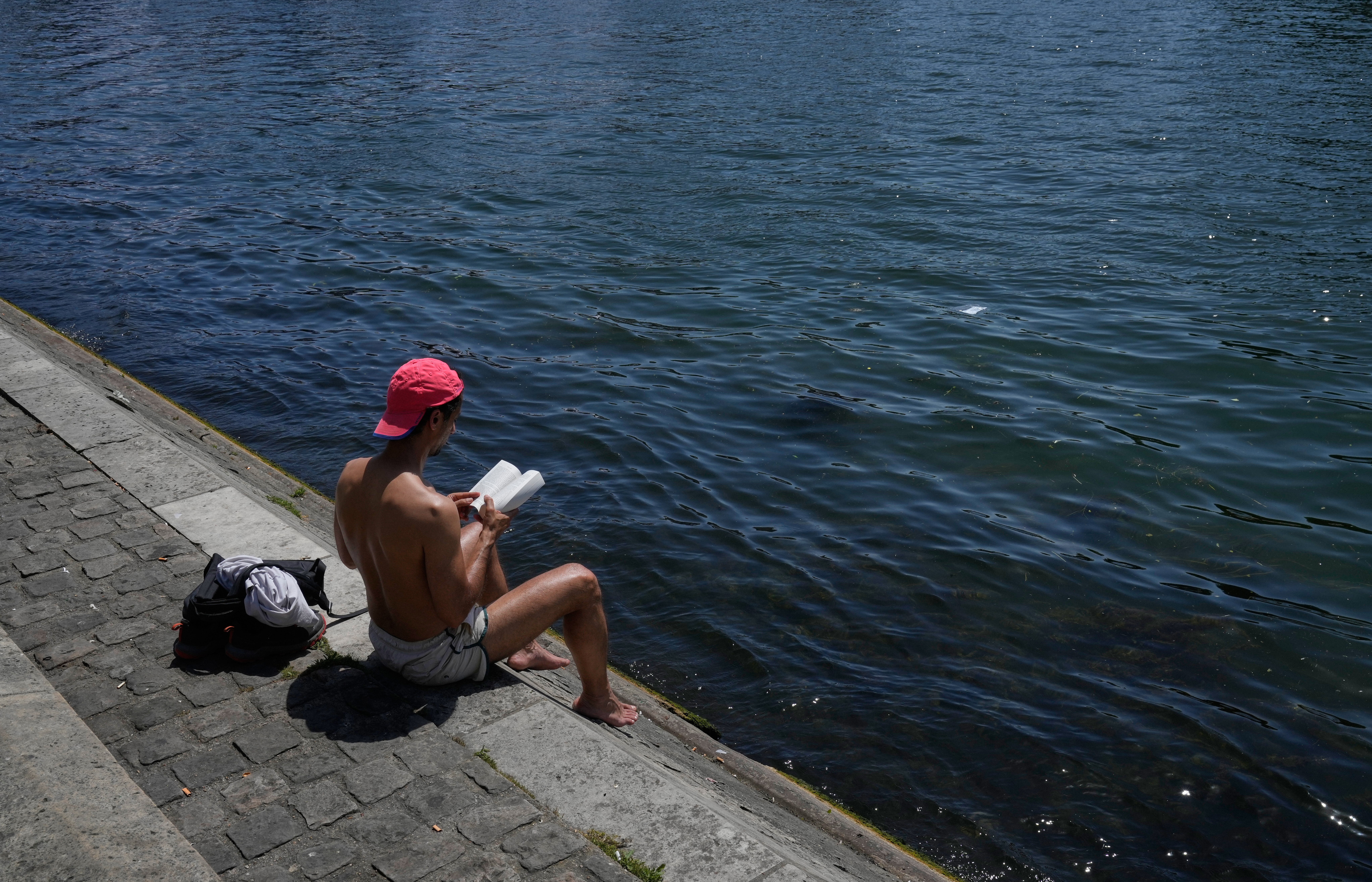 Un hombre sentado leyendo un libro bajo el sol a orillas del río Sena, el lunes 25 de mayo de 2026, en París. (Foto AP/Michelle Euler)