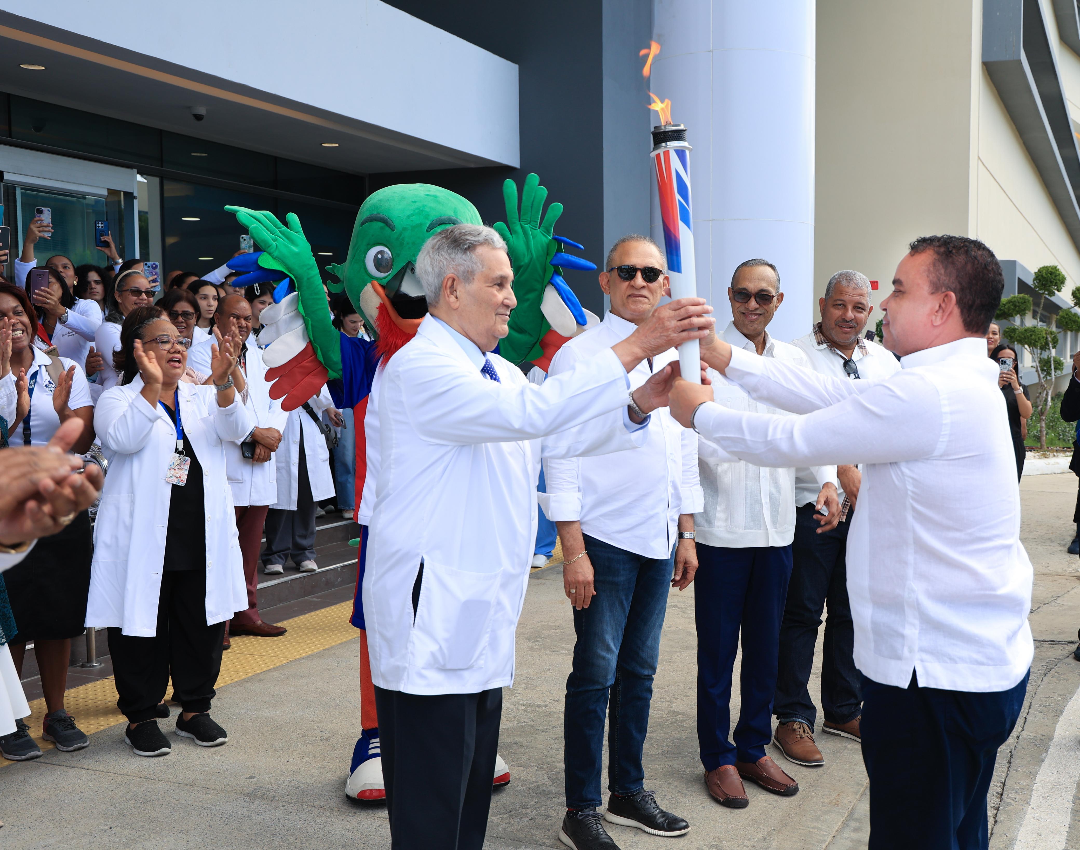 Julio Landrón recibe la antorcha de Santo Domingo 2026 en la Ciudad Salud de Luis Eduardo Ibar junto a médicos y autoridades del sistema de salud.