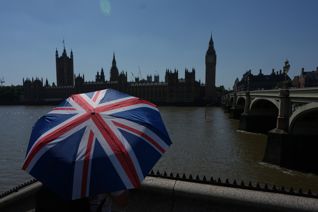 Un turista posa para una fotografía usando un paraguas con la bandera británica, en Londres, el 24 de junio de 2026. (Foto AP/Alistair Grant)