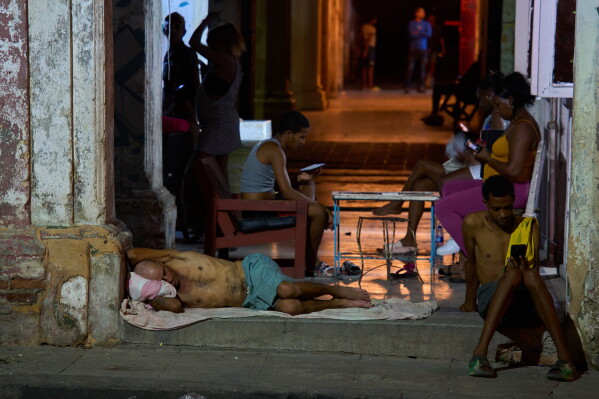 Un hombre duerme en la puerta de su casa mientras otros pasan el tiempo tratando de refrescarse en la calle en La Habana, Cuba, el martes 4 de agosto de 2026.